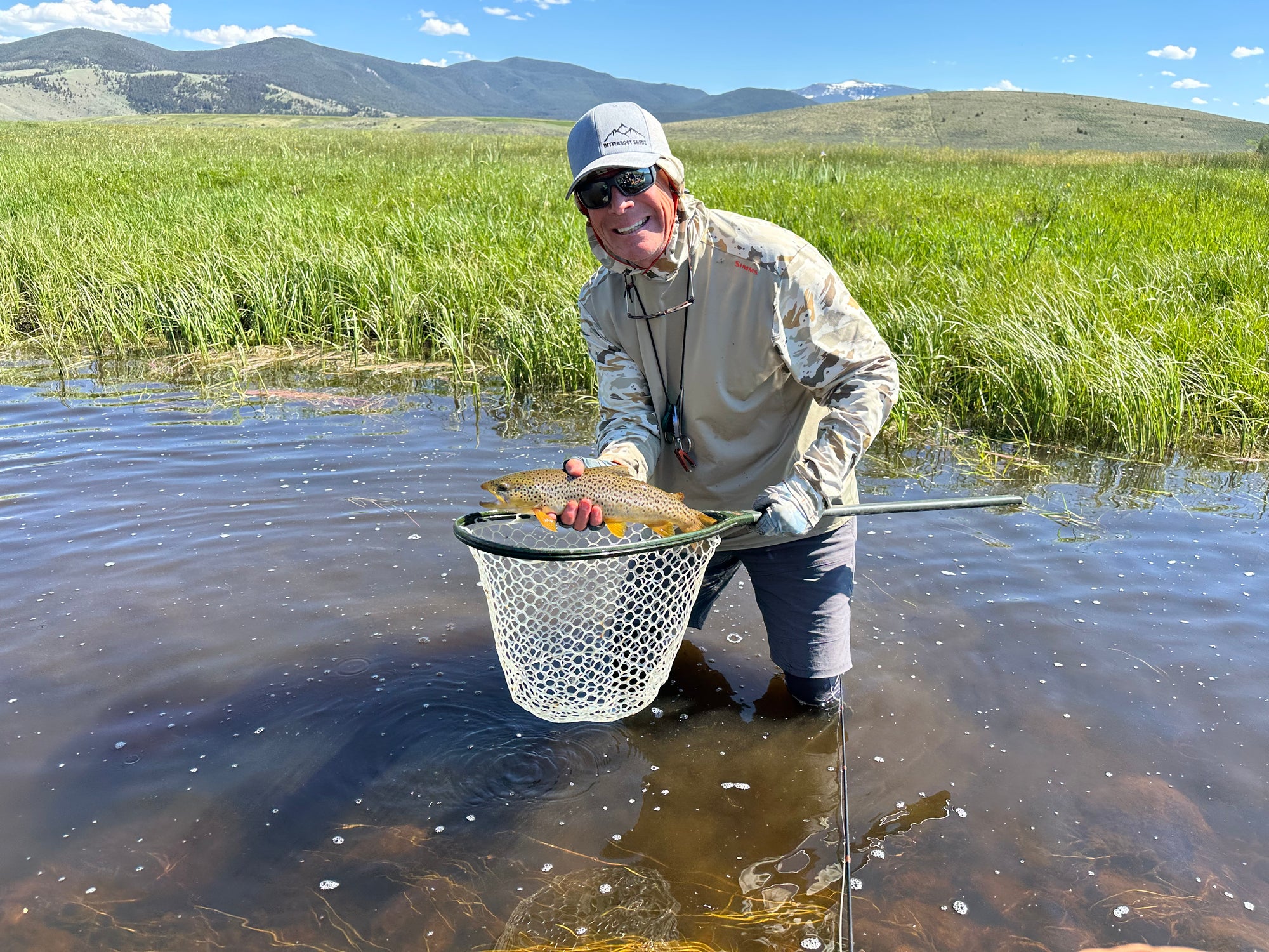 Guide holding a fish and fishing net in a marshy area with mountains in the background